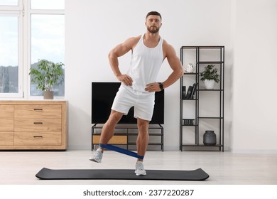 Athletic man doing exercise with elastic resistance band on mat at home