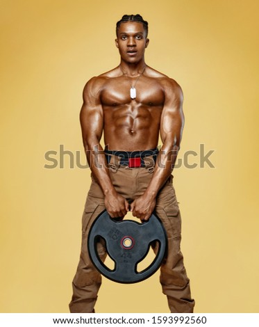 Athletic man doing exercise with heavy weights disc. Photo of man with naked torso and good physique on yellow background. Strength and motivation