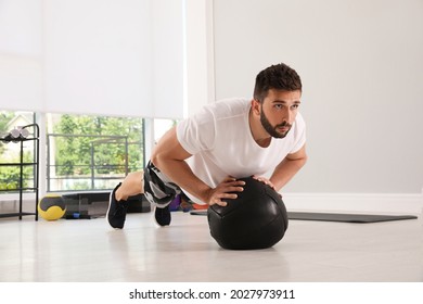Athletic man doing push ups with medicine ball in modern gym