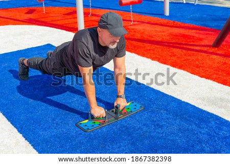 Athletic man doing push-ups on a push-up board at the sports field in the city park.