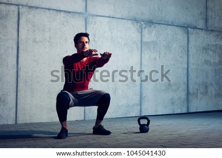 Athletic man doing squats preparing to do kettlebell exercises
