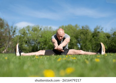 Athletic Man Doing Stretching Exercises Outdoors in Nature.Male Fitness Enthusiast Performing Wide-Leg Stretch on Grass.Sporty Man Stretching Legs in Open Field on a Sunny Day.