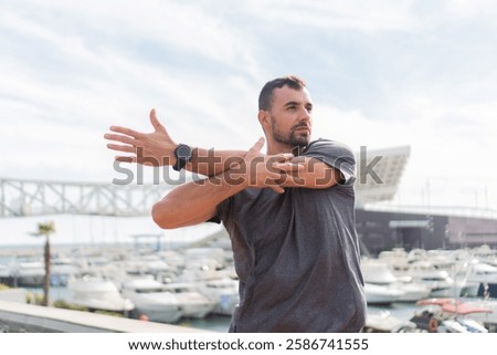 Athletic Man Engaging in Dynamic Stretching Exercise by the Marina While Wearing Sporty Attire to Enhance Flexibility and Prepare for an Energetic Workout Session with a Focus on Physical Fitness Goal