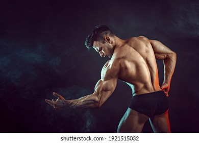 Athletic man flexing muscles in studio on dark background with smoke. Strong bodybuilder with perfect abs. - Powered by Shutterstock