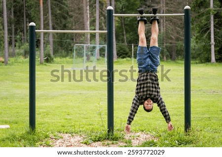 Athletic man in gravity boots hangs on a horizontal bar outdoors on a summer day. Healthy lifestyle.