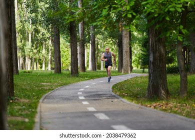 Athletic Man Long Distance Runner Training In The Park Alleys