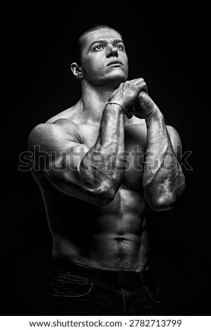 Athletic man looking up with intense focus in low key lighting. Muscular body, strength and motivation concept, fitness and bodybuilding, dramatic shadows on dark background.