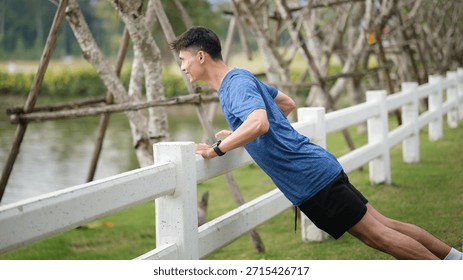 Athletic man performing push-up exercise using park fence. Outdoor workout and healthy lifestyle concept.