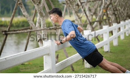 Athletic man performing push-up exercise using park fence. Outdoor workout and healthy lifestyle concept.