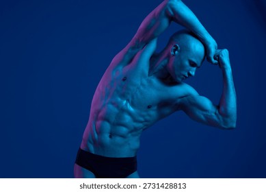 Athletic man posing in dramatic blue lighting, showcasing his impressive physique and strength. This striking image captures the essence of fitness and dedication.