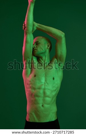 Athletic man posing gracefully under dramatic green lighting, showcasing strength and artistry in this dynamic capture. Emphasizing the beauty of form and movement.