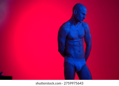 Athletic man posing in low light, showcasing toned physique against a vibrant red background. Captivating and striking imagery with bold colors and dramatic lighting.