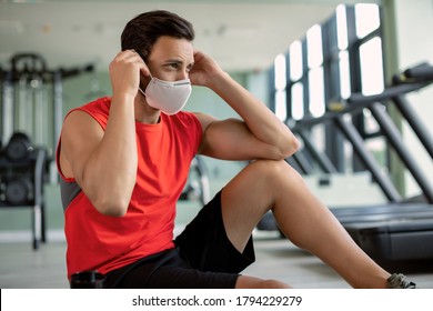 Athletic Man Preparing For Workout And Putting On Protective Face Mask In A Health Club Due To Coronavirus Epidemic. 