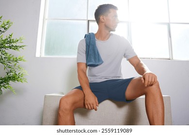 Athletic Man Resting Indoors with Towel Over Shoulder, Sunlit Minimalist Setting and Relaxed Post-Workout Vibe - Powered by Shutterstock