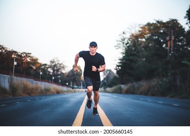 Athletic Man Runner Work Out On Street. Sportive Asian Male Running In The Middle Of The Road And Looking At Camera. Healthy Lifestyle