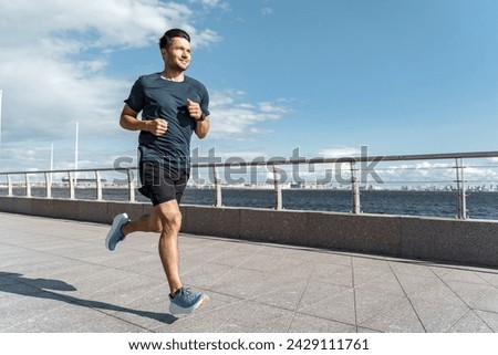 Athletic man running on a waterfront promenade with a clear sky, personifying dedication and a healthy, active lifestyle.