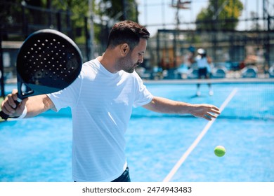 Athletic man serving the ball while playing paddle tennis on the court. Copy space. - Powered by Shutterstock