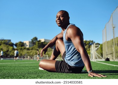 Athletic man soccer player wear blue athletic tank top and black shorts sitting on grassy sports football field, resting after game or workout, look aside. Take a break, sports, lifestyle - Powered by Shutterstock