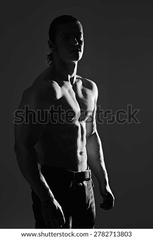 Athletic man standing in dramatic lighting, strong muscular body highlighted by shadows. Fitness and bodybuilding concept, masculine strength, dark background with copy space.