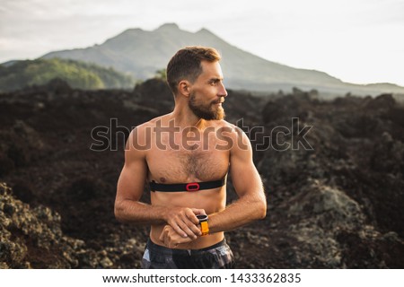 Athletic man start running program on smart watch or fitness tracker. Training topless and using chest heart rate monitor. Trail running outdoors.
