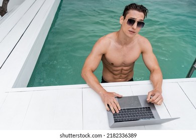 Athletic Man In Sunglasses Using Laptop At Poolside