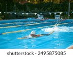 Athletic man, swimmer in white swim cap and goggles swims laps in pool, showcasing his dedication to training outdoor. Concept of professional sport, competition, active and healthy lifestyle. Ad