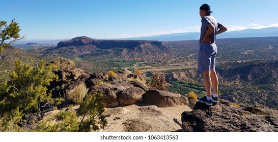 Athletic Man Taking a Break While Standing on Edge of a Tall, Rocky Cliff and Overlooking Panoramic and Scenic View of Mountains, Plateaus and Valleys on a Crisp, Clear Day