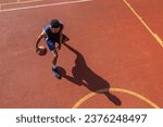 Athletic man training basketball at outdoor court.