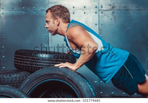 Athletic man trains, pushed from a\
car tire forward looking. concept of health and\
strength.