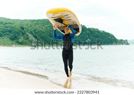 An athletic man in a wetsuit carries a SUP board on his head along the sandy seashore. Extreme recreation. 商業照片 © 