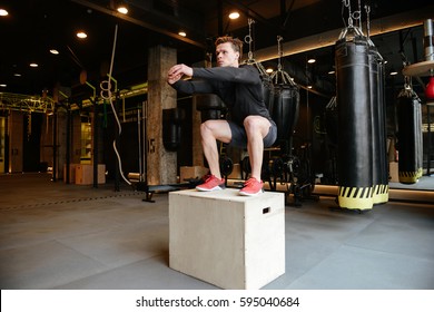 Athletic man which jumping on box in gym
