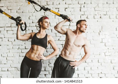 Athletic Man And Woman Doing TRX Workout At Gym.