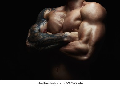 Athletic man's torso. Unrecognizable male fitness model show naked muscular body. Strong hands, chest and shoulder muscles and biceps. Studio shot on black background, low key. Bodybuilding concept