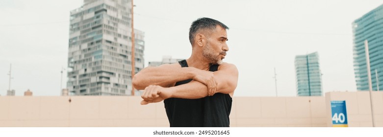 Athletic mature man stretches arm muscles while standing on the beach in the morning - Powered by Shutterstock