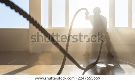 athletic men with battle rope in functional training fitness gym. crossfit exercises concept image