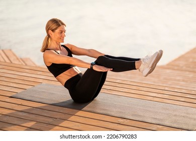 Athletic Middle Aged Woman Making V-Up Abs Workout Outdoors, Sporty Smiling Woman Training On Wooden Pier Near River, Exercising On Fitness Mat Outside, Enjoying Healthy Lifestyle, Copy Space