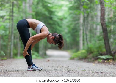 Athletic middle aged woman stretching in the green leaved woods on a dirt road before a run in Surry, Maine, USA during the Summer.