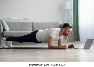 Athletic middle-aged man in sportswear planking in front of laptop, having online fitness class from home, living room interior, copy space. Sporty bearded man enjoying daily exercising - Powered by Shutterstock