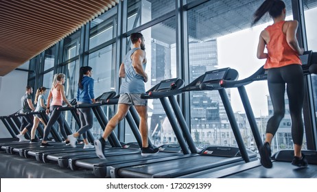 Athletic Muscular Man Running on a Treadmill, Leg and Cardio Day. Strong Man Training in the Modern Gym Fitness Club with Window Cityscape View. Back View Shot