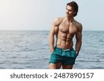 Athletic, muscular man in swim shorts posing at the beach.

