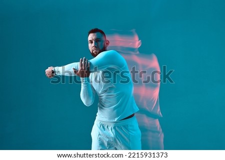 Athletic muscular young guy fitness trainer stretching arm muscle. Warm up exercise. Sports workout. Long exposure