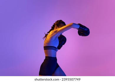 Athletic and powerful, young woman in boxing attire stands out against gradient pink-violet studio background in neon light. Concept of sport, active lifestyle, health, competition, championship. - Powered by Shutterstock