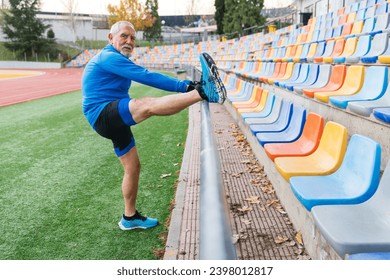 Athletic senior man stretching on track field, vibrant empty bleachers in background, cloudy day - Powered by Shutterstock