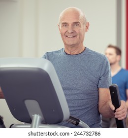 Athletic Senior Man Working Out A Gym On The Exercise Equipment Looking At The Camera With A Friendly Happy Smile