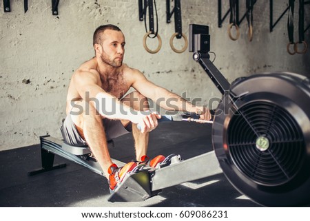Athletic shirtless male doing workouts on a back with power exercise machine in a gym club.