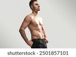 Athletic shirtless man striking a confident pose with hands on hips, wearing jeans. Emphasis on fitness and strength.