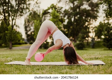 athletic, slender woman in pink clothes and small rubber ball doing Pilates on pink mat at dawn in park in summer. 
