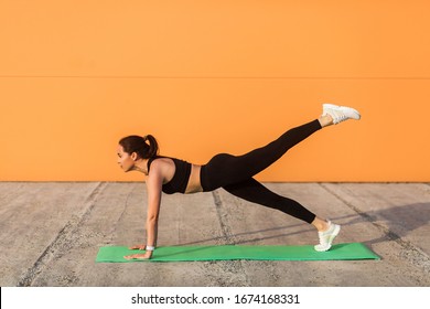 Athletic Slim Young Woman In Sportswear, Black Pants And Top, Practicing Yoga, Standing In Phalakasana Higher Plank Pose With Leg Lift, Training Muscles, Flexibility. Health Care, Sport Activity