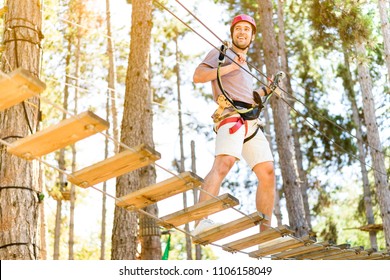 Athletic Sporty Guy Doing Activity In Adventure Park With All Climbing Equipment Like Helmet, Rope And Carabiner. Active People Climb On The Trees And Having Fun Outdoors Enjoying Nature Landscape. 
