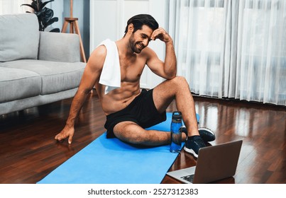 Athletic and sporty man resting on fitness mat during online body workout exercise session for fit physique and healthy sport lifestyle at home. Gaiety home exercise workout training concept. - Powered by Shutterstock